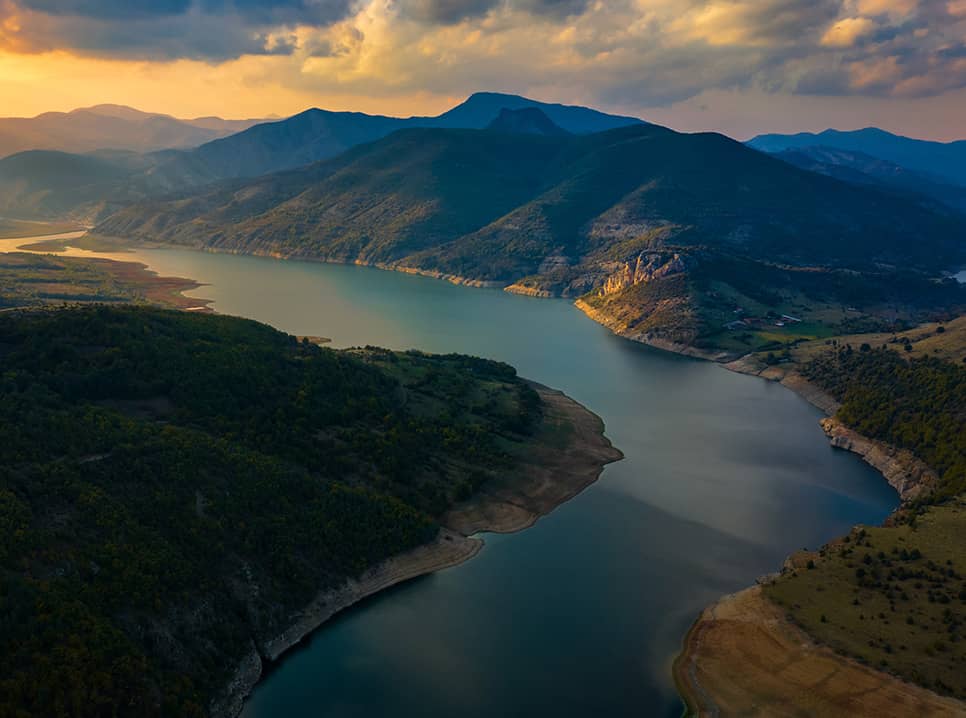 An aerial photos showing a large river and mountains as the sun is setting