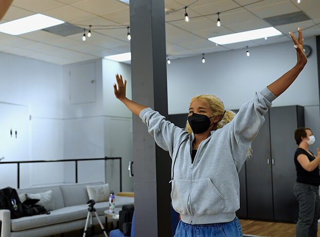 A person stands with their arms raised and out in an LGBTQ drama therapy documentary called River of Life by Grace Walcott